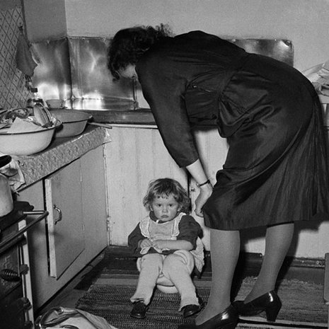 Perhejuhla kotona 1950-luvulla, pieni tyttö istuu keittiössä potalla, äiti seisoo vieressä. Kuva: Väinö Kannisto / Helsingin kaupunginmuseo