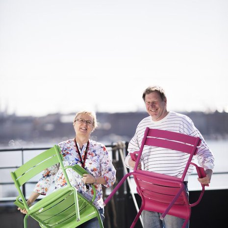 Leena Vahtera asettelee tuoleja Kotisataman kattoterassilla. Mukana puuhassa toinen talon asukas, Jorma Kaunismäki.
