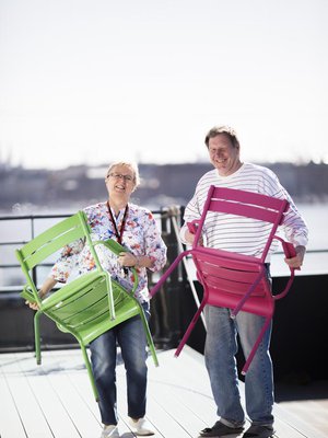 Leena Vahtera asettelee tuoleja Kotisataman kattoterassilla. Mukana puuhassa toinen talon asukas, Jorma Kaunismäki.