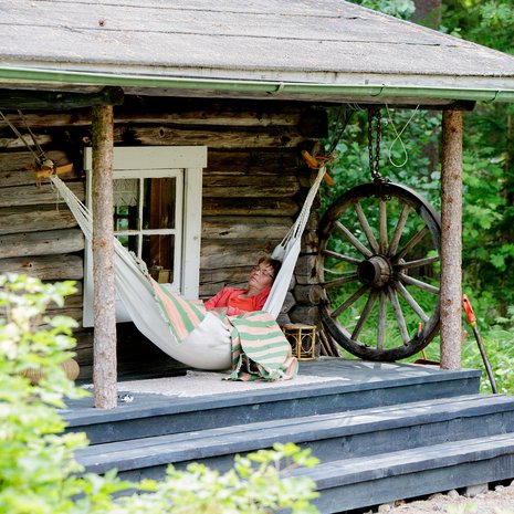 Anja Hokkanen ottaa päivänokosia leikkimökin terassilla. Mökki on tehty vanhasta savusaunasta. 