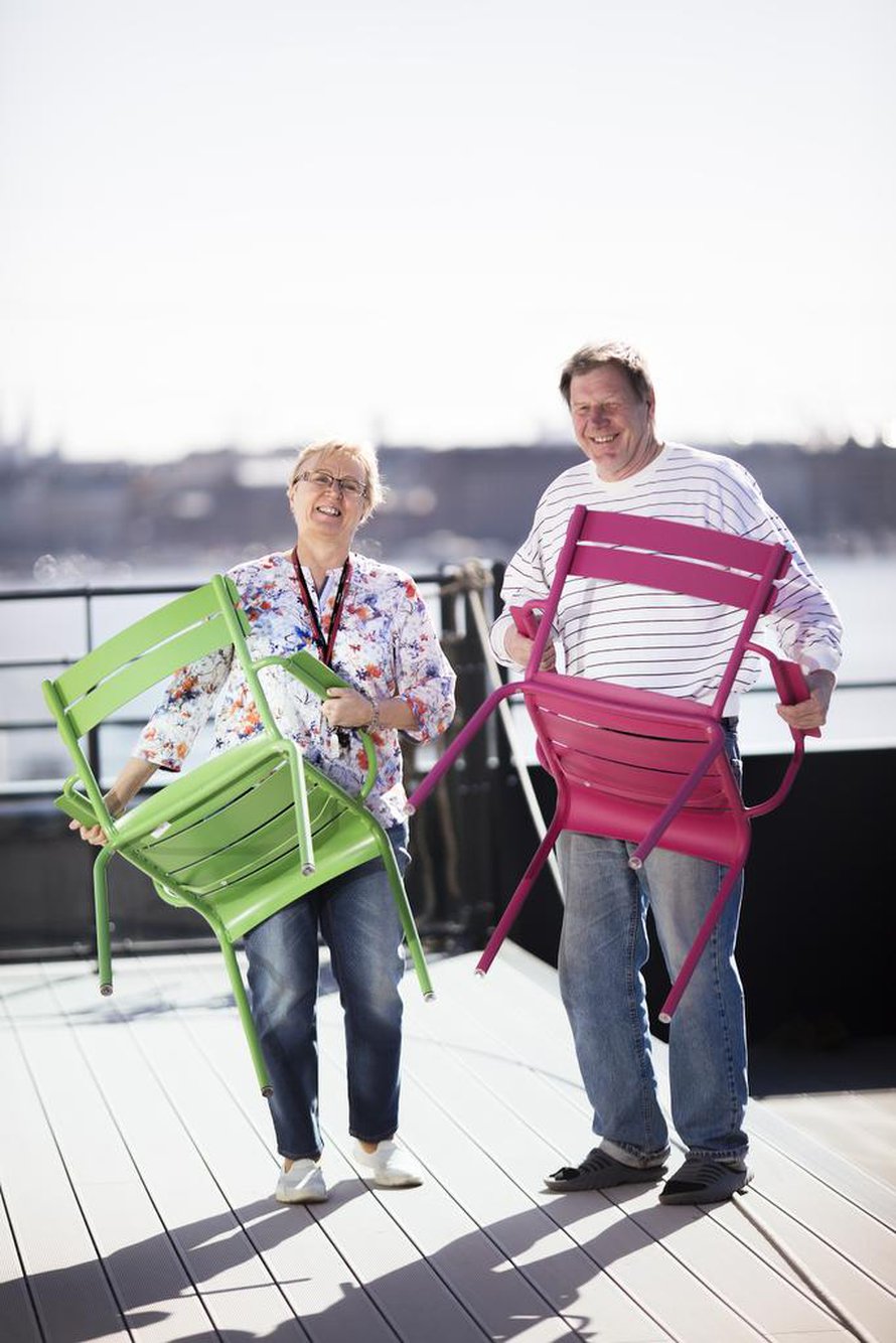 Leena Vahtera asettelee tuoleja Kotisataman kattoterassilla. Mukana puuhassa toinen talon asukas, Jorma Kaunismäki.