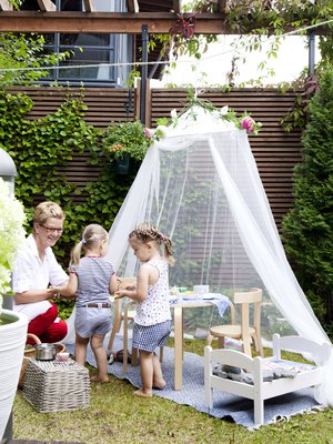 Alisa ja Ellen tarjoavat Anne-mummille kahvia prinsessalinnassa. Kevyt maja on nopea rakentaa, ja sateen sattuessa sen voi siirtää lasitetun terassin suojaan.